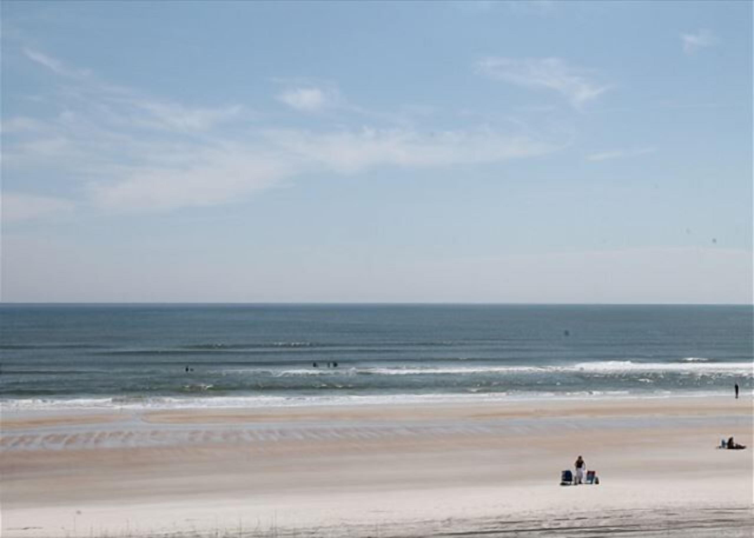 A beach with a wide sandy shore, a clear sky, and a calm sea.