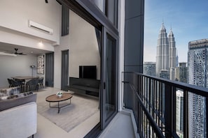A modern living room with a sofa, coffee table, and TV, overlooking a cityscape with tall buildings. - Isola Klcc Hotel, Trademark Collection By Wyndham (Kuala Lumpur)