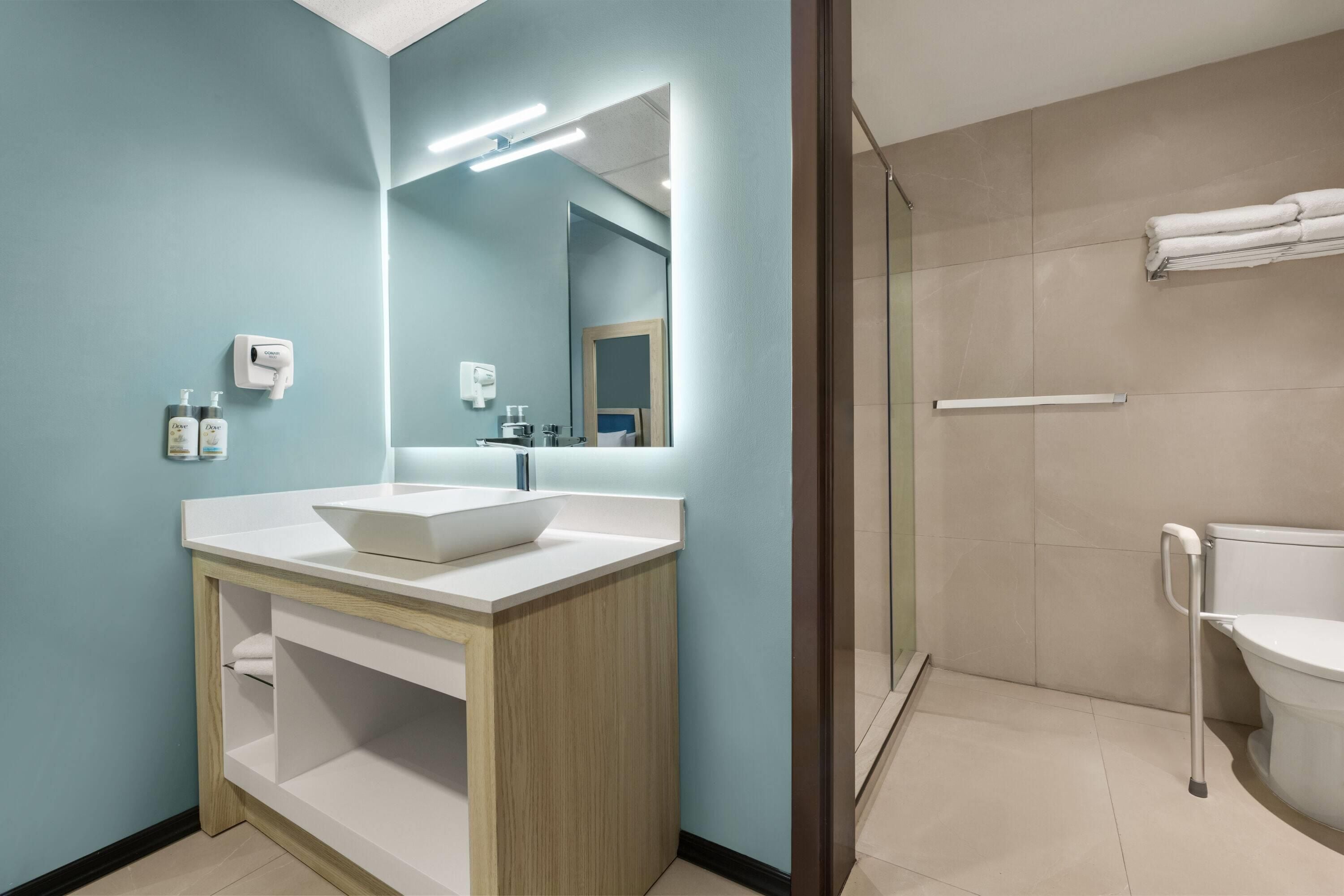 Casa de banho moderna com lavatório branco, espelho e zona de duche.