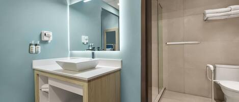A modern bathroom with a white sink, a mirror, and a shower area.