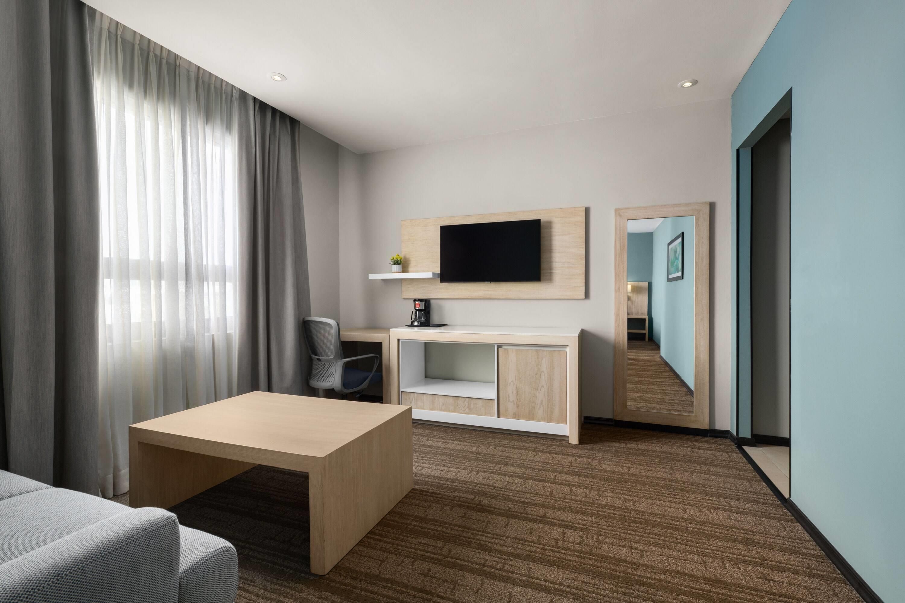 A hotel room with a bed, a desk, a chair, a TV, and a mirror.