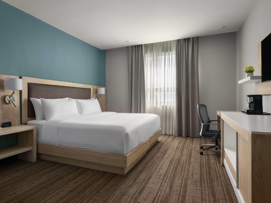 A hotel room with a bed, bedside tables, a desk, a chair, a television, and a coffee maker.