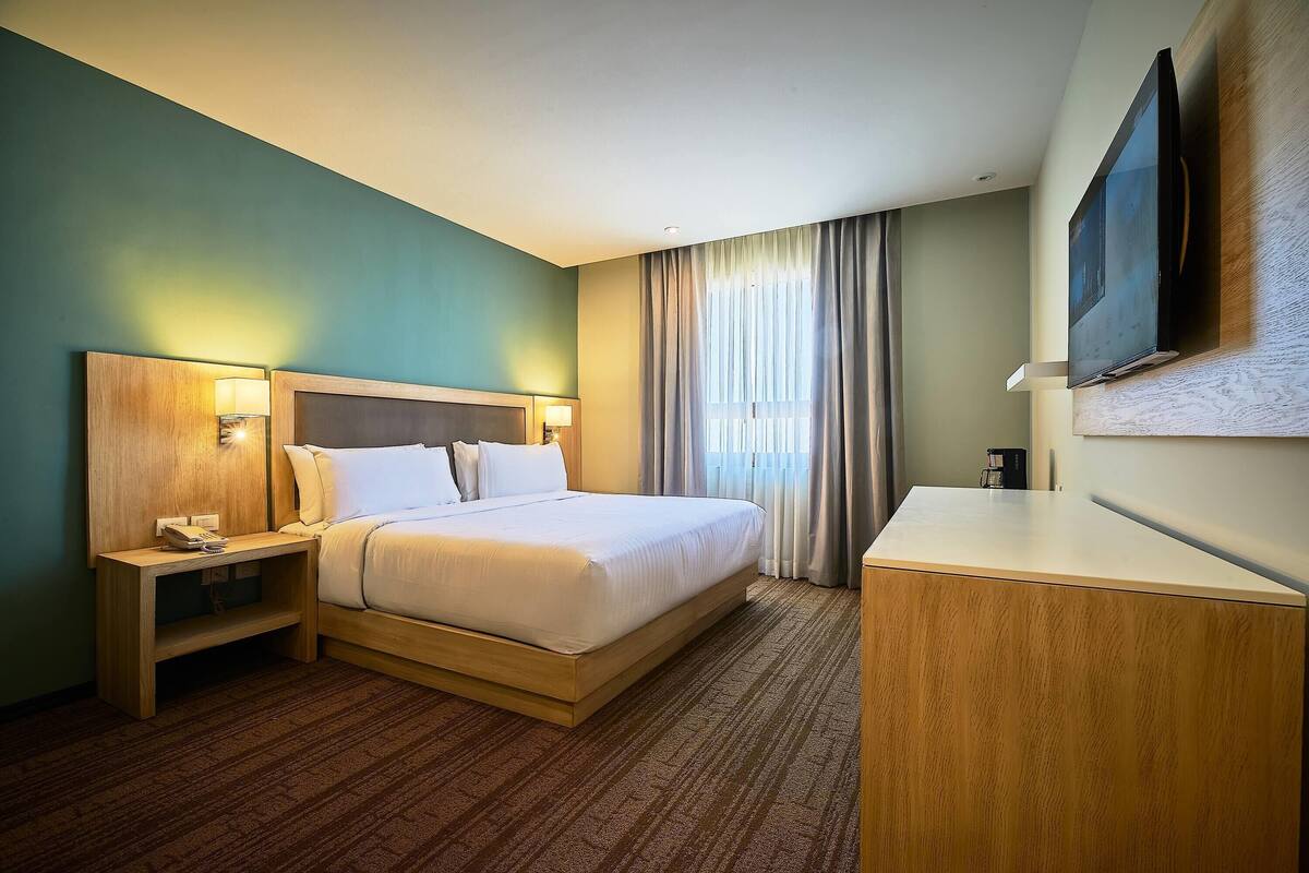 A hotel room with a bed, bedside tables, a TV, and a desk.