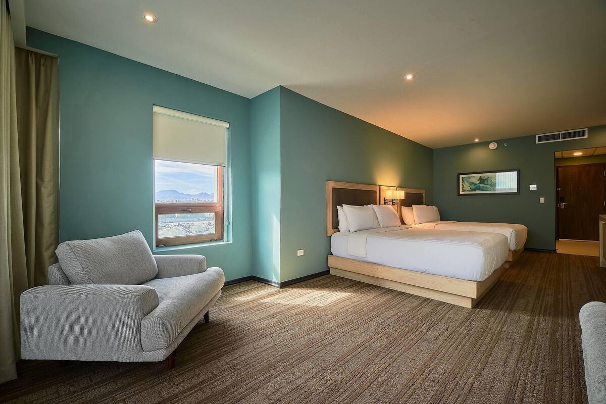 A hotel room with a large bed, a sofa, a window with a view, and a carpeted floor.