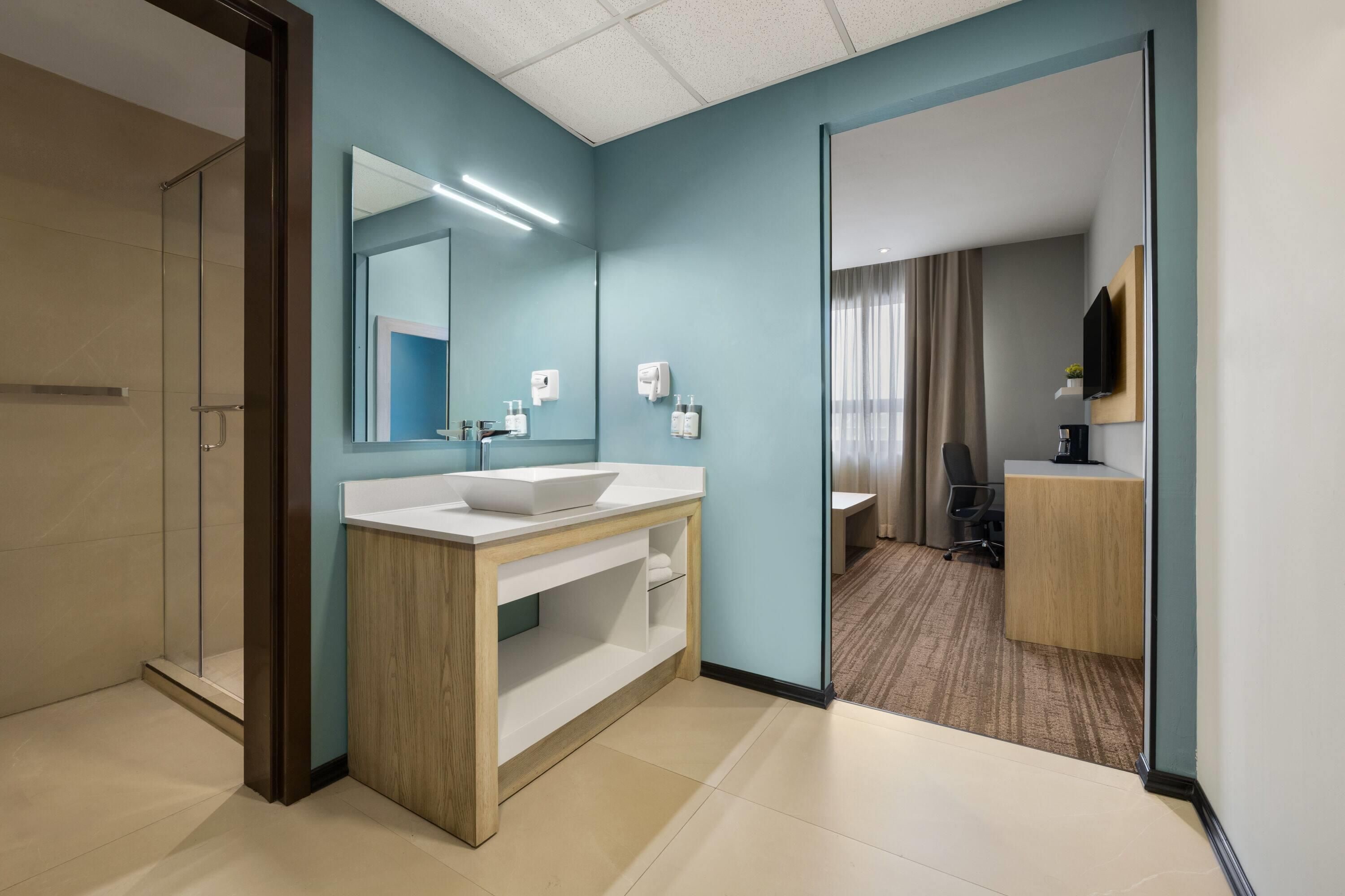 Un baño de hotel con un espejo grande, un lavamanos y una ducha.