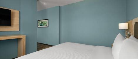 A hotel room with a bed, a mounted TV, a bedside lamp, and a framed picture on the wall.