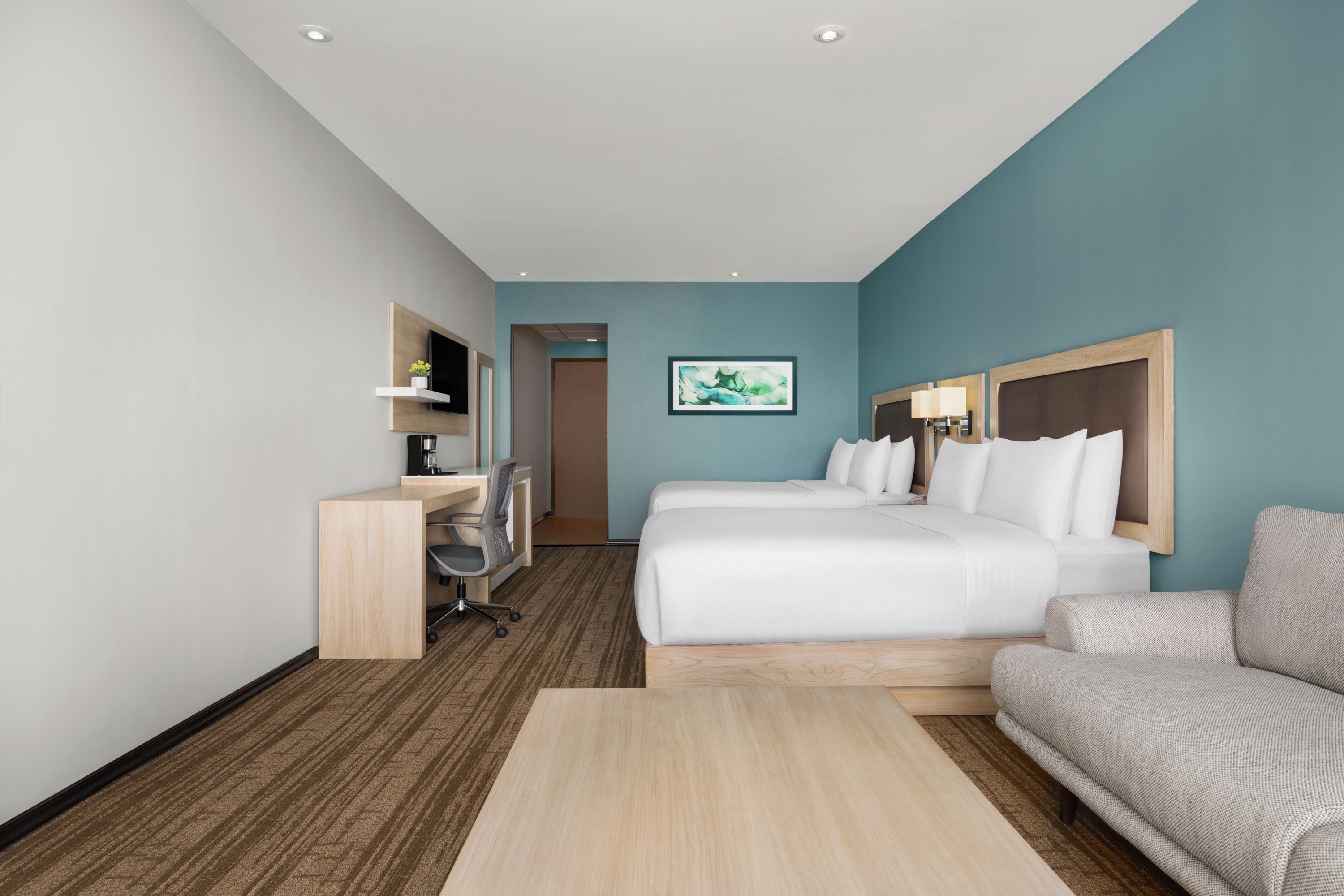 Una habitación de hotel con una cama, un escritorio, una silla, un sofá y un cuadro en la pared.