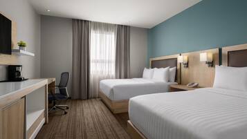 Habitación de hotel con dos camas, un escritorio con cafetera, una silla y un ventanal con cortinas.