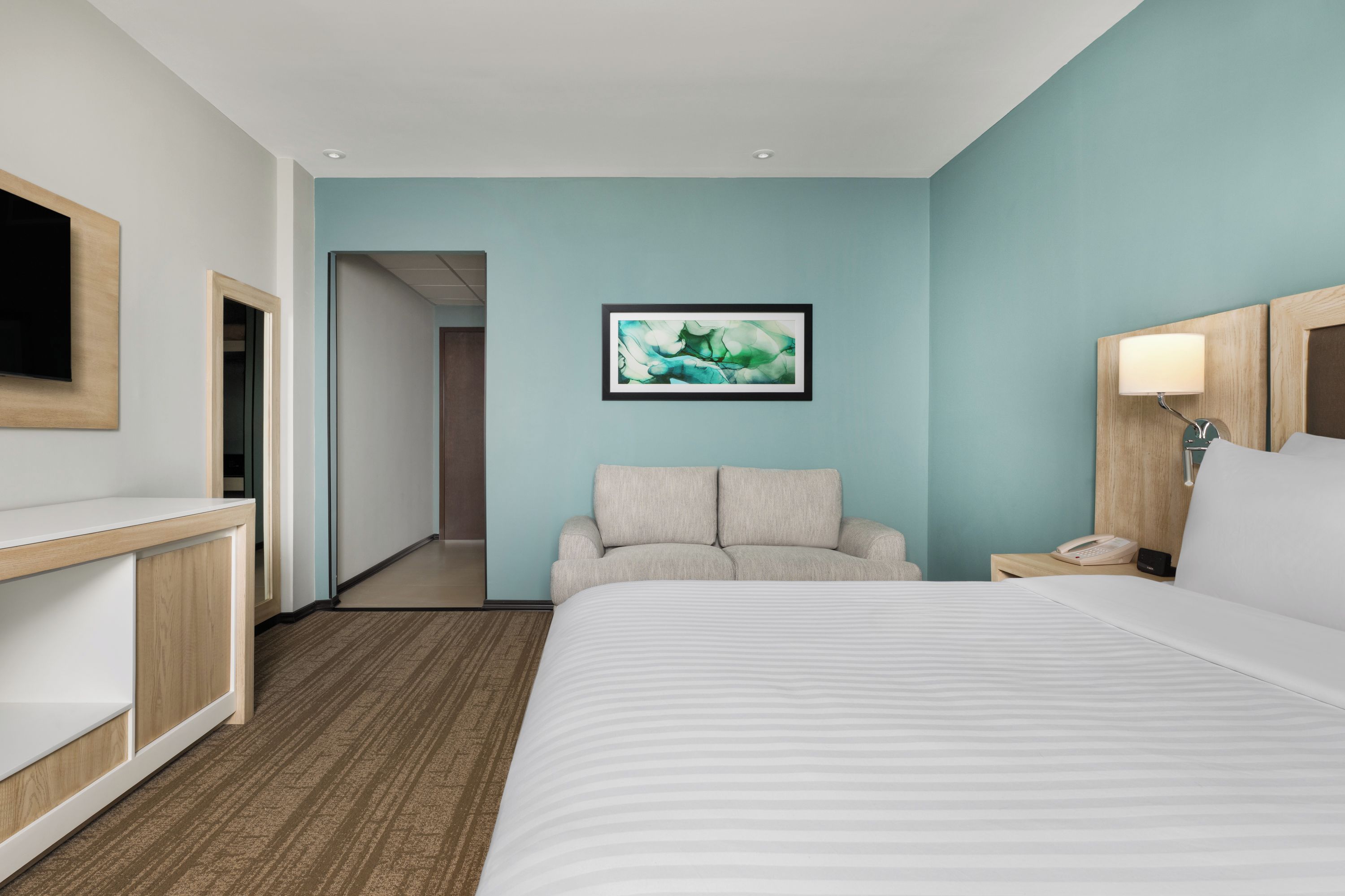 Quarto de hotel com cama, área de estar, escrivaninha e televisão.