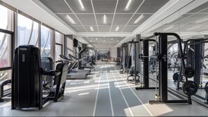 Un gimnasio moderno con máquinas de cardio, equipo de levantamiento de pesas y una vista despejada de la ciudad a través de amplias ventanas.