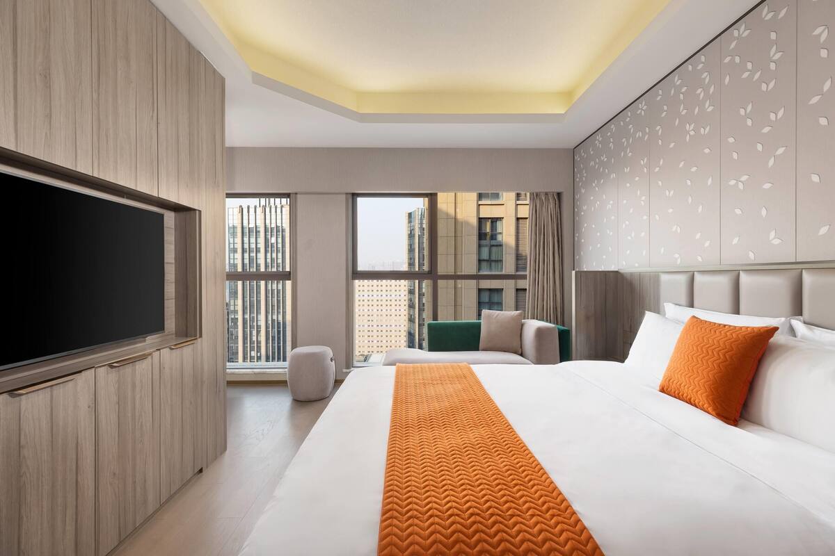 Een moderne hotelkamer met een groot bed, een flatscreen televisie en stadszicht door de ramen.