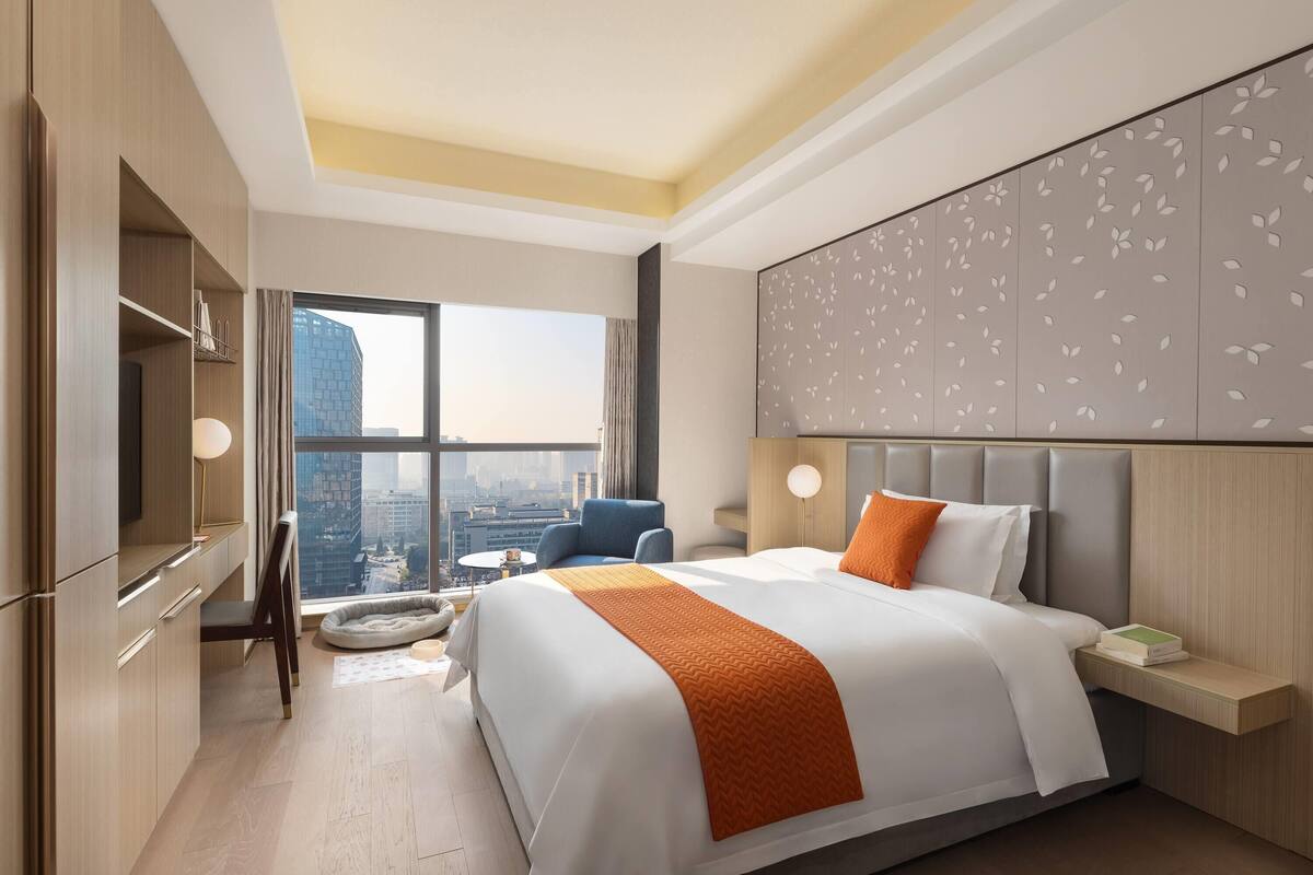 Een moderne hotelkamer met een groot bed, een bureau en uitzicht op de stad.