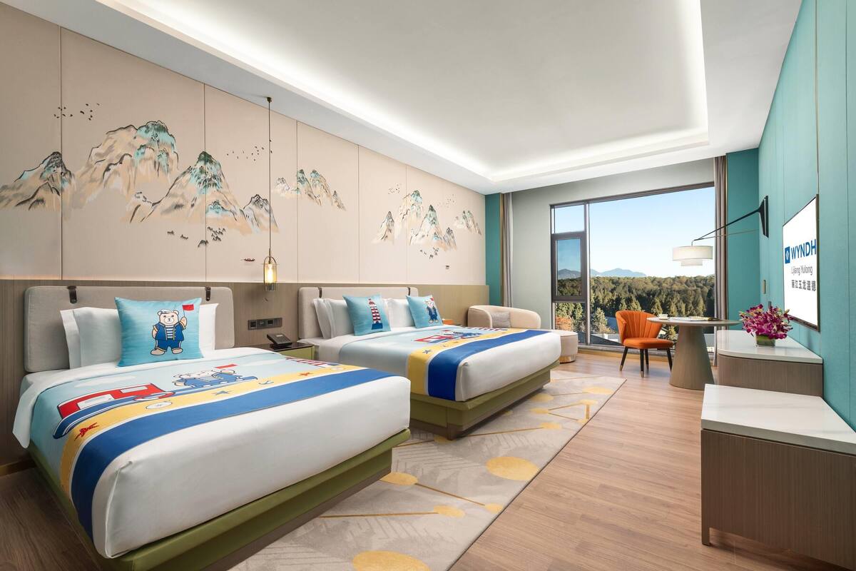 A hotel room with two beds, a desk, a chair, a large window, and a painting on the wall.