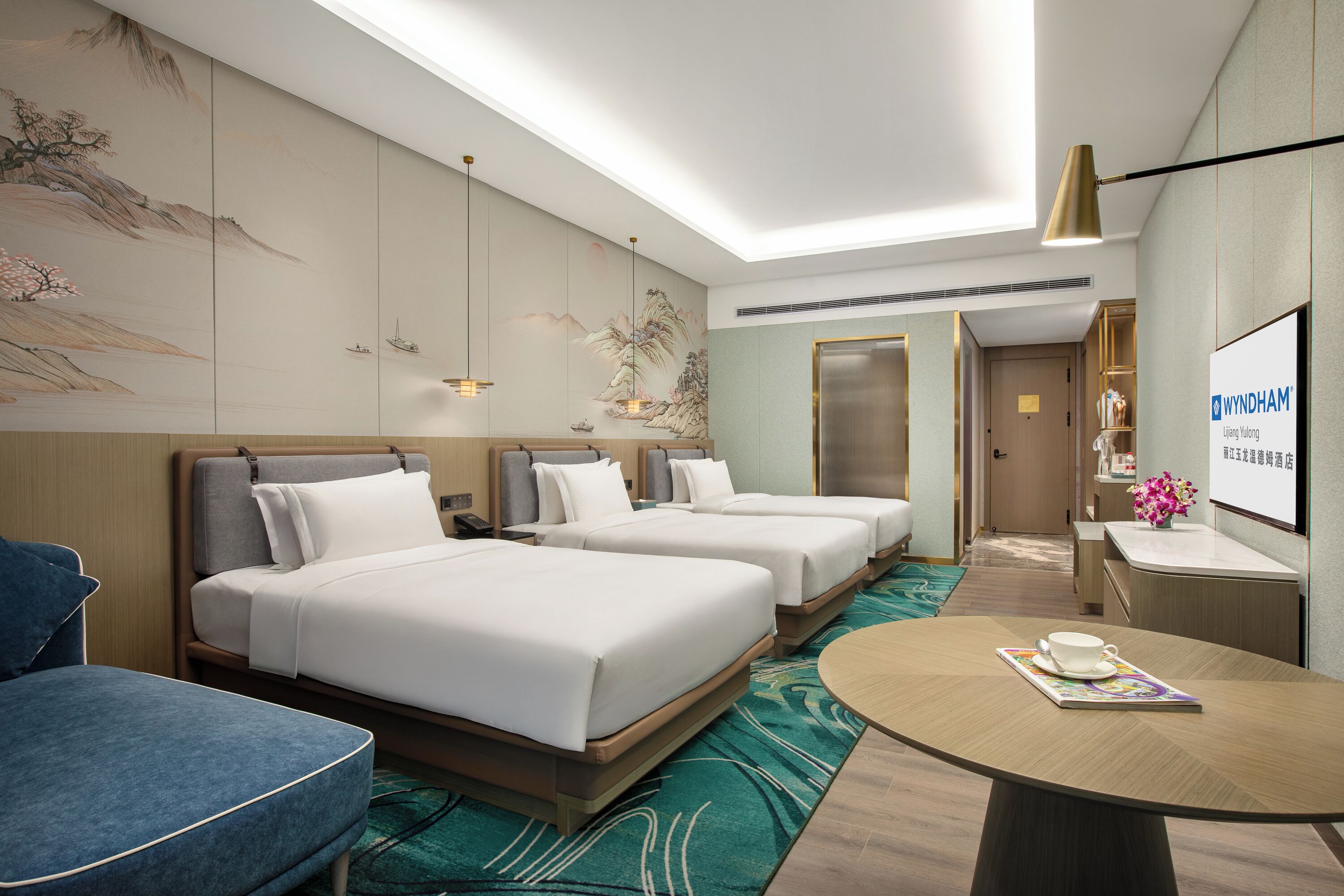 A hotel room with two beds, a desk, a chair, and a round table with a cup and saucer.