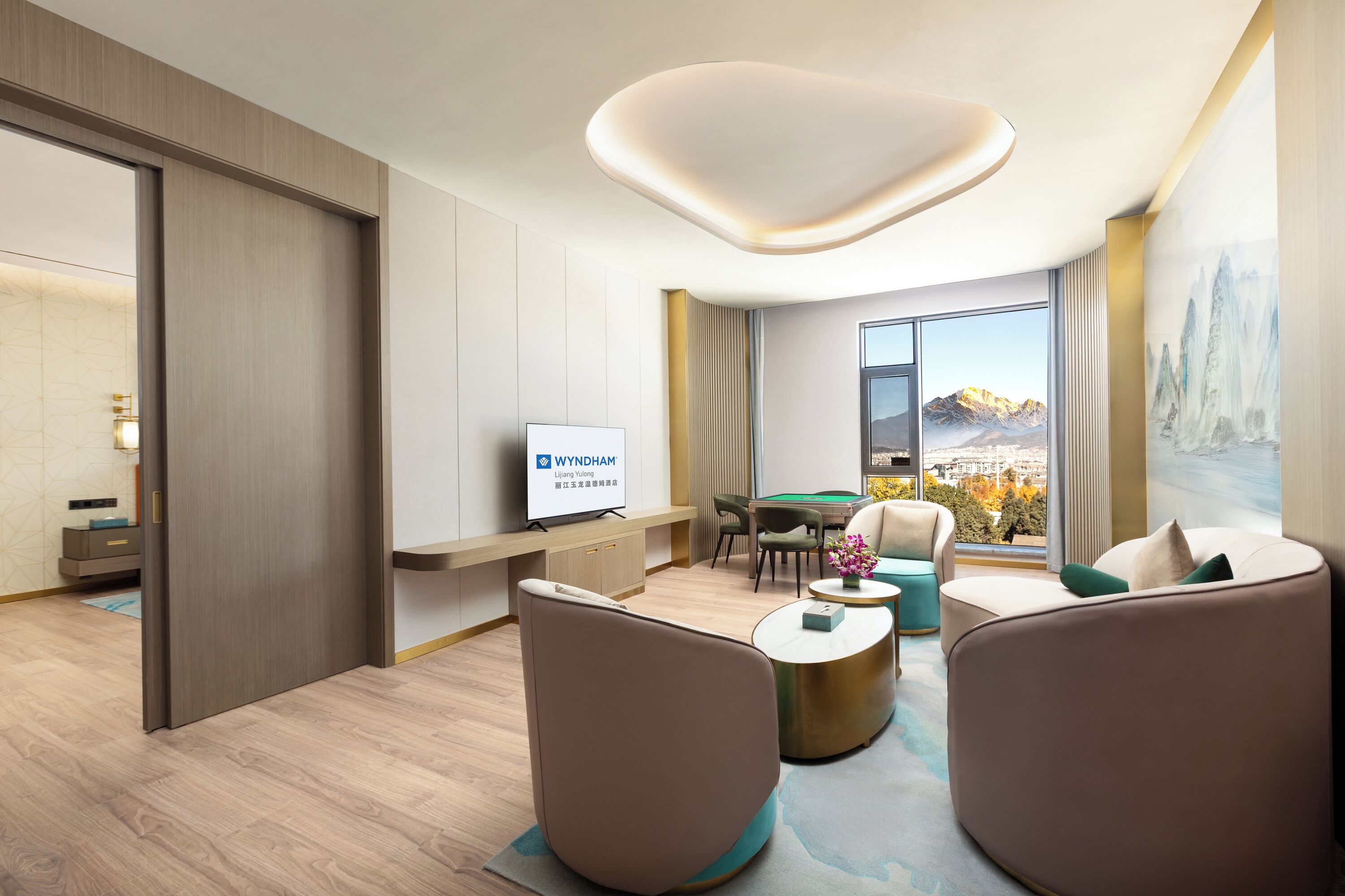 A modern hotel room with a pool table, comfortable seating, a television, and a large window with a mountain view.