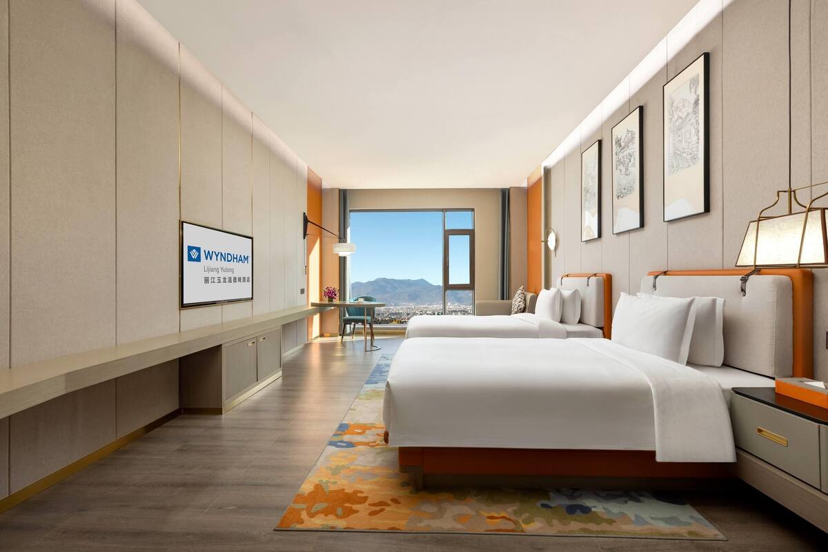 A hotel room with a large bed, a desk, a chair, and a view of the mountains.