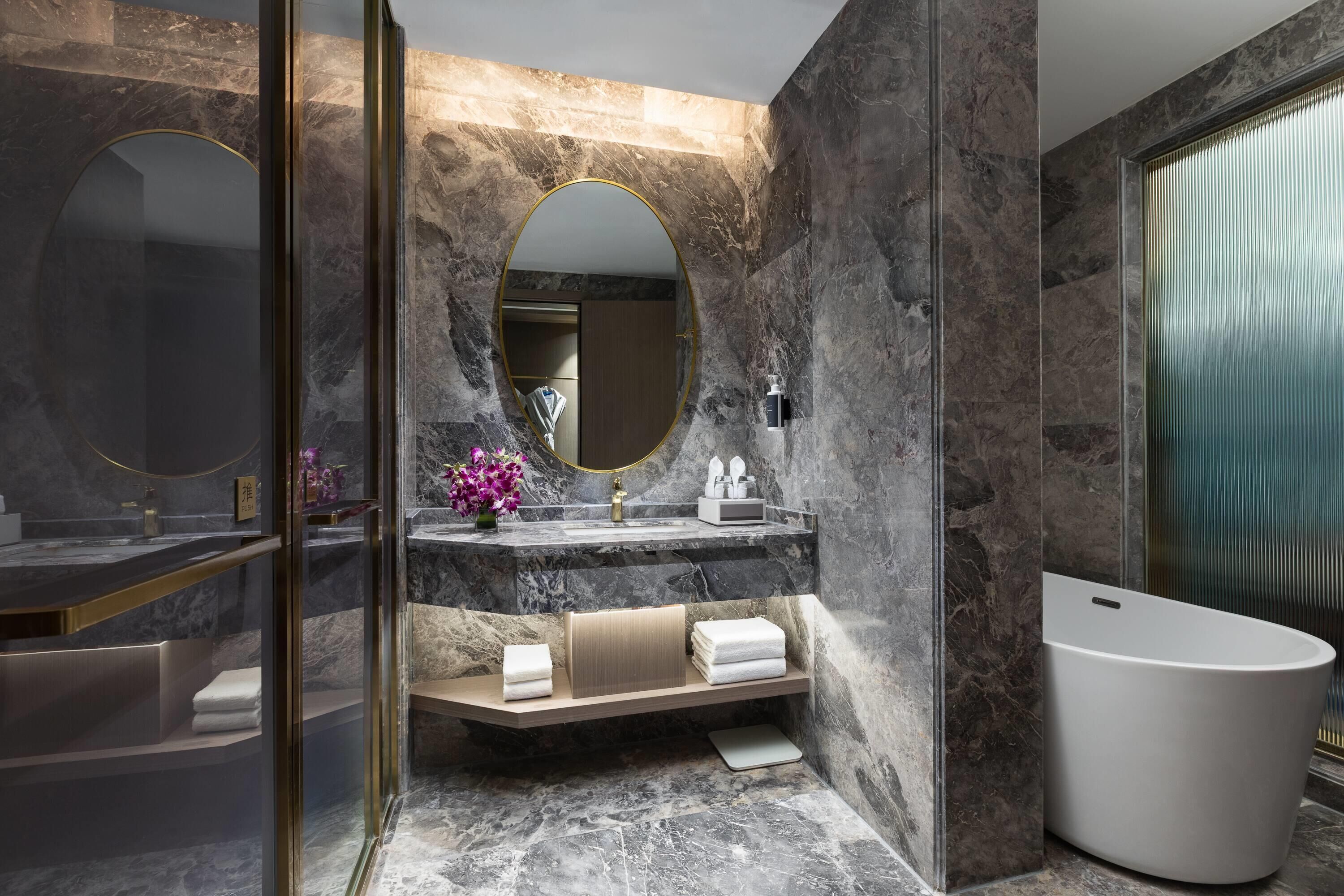 Un baño moderno con pared de mármol, una bañera independiente, un tocador con espejo y un perchero para toallas.