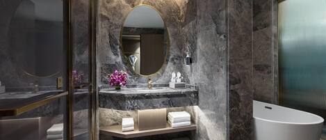 Un baño moderno con pared de mármol, una bañera independiente, un tocador con espejo y un perchero para toallas.