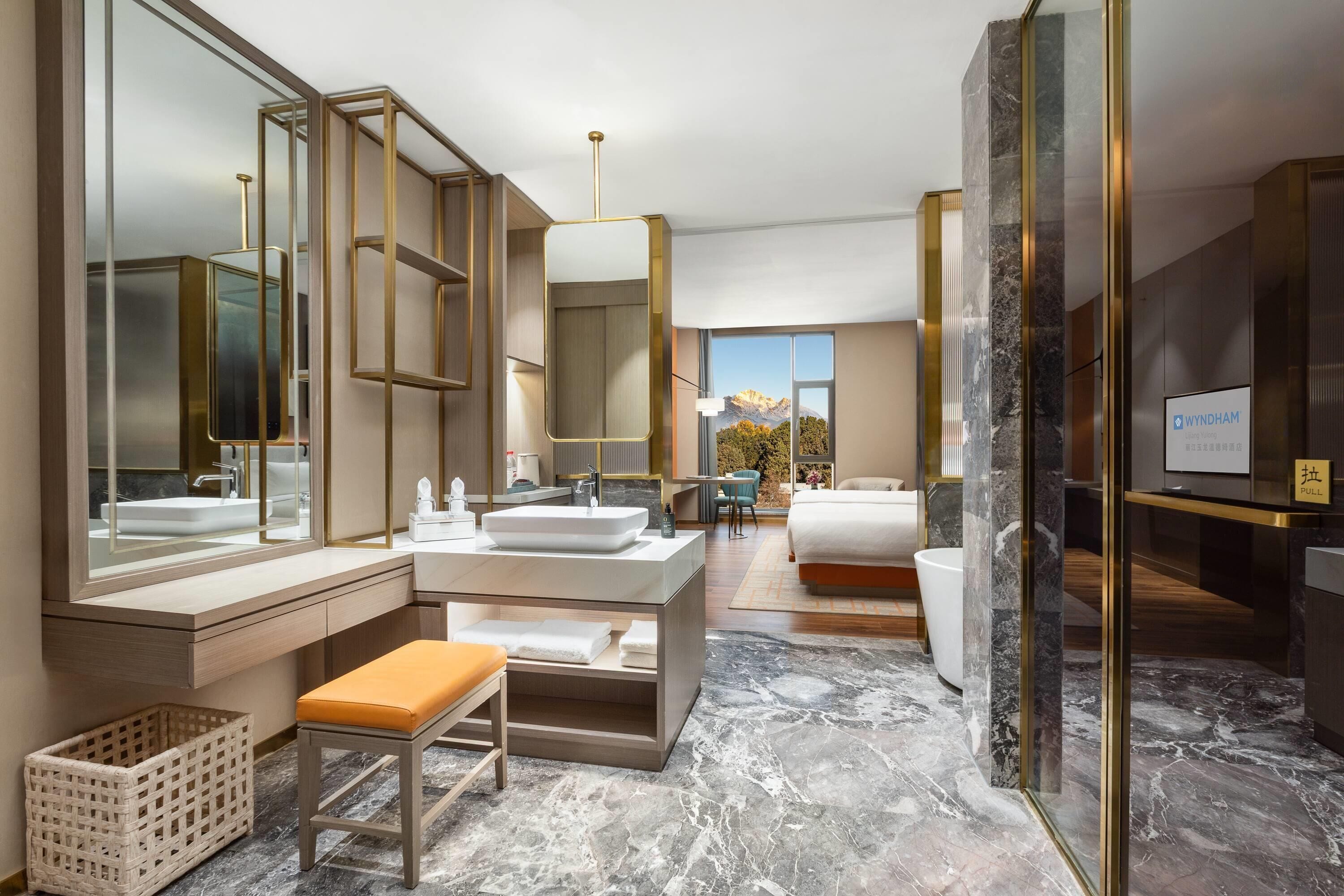 Un baño de hotel moderno con un espejo grande, un lavamanos y un banco.
