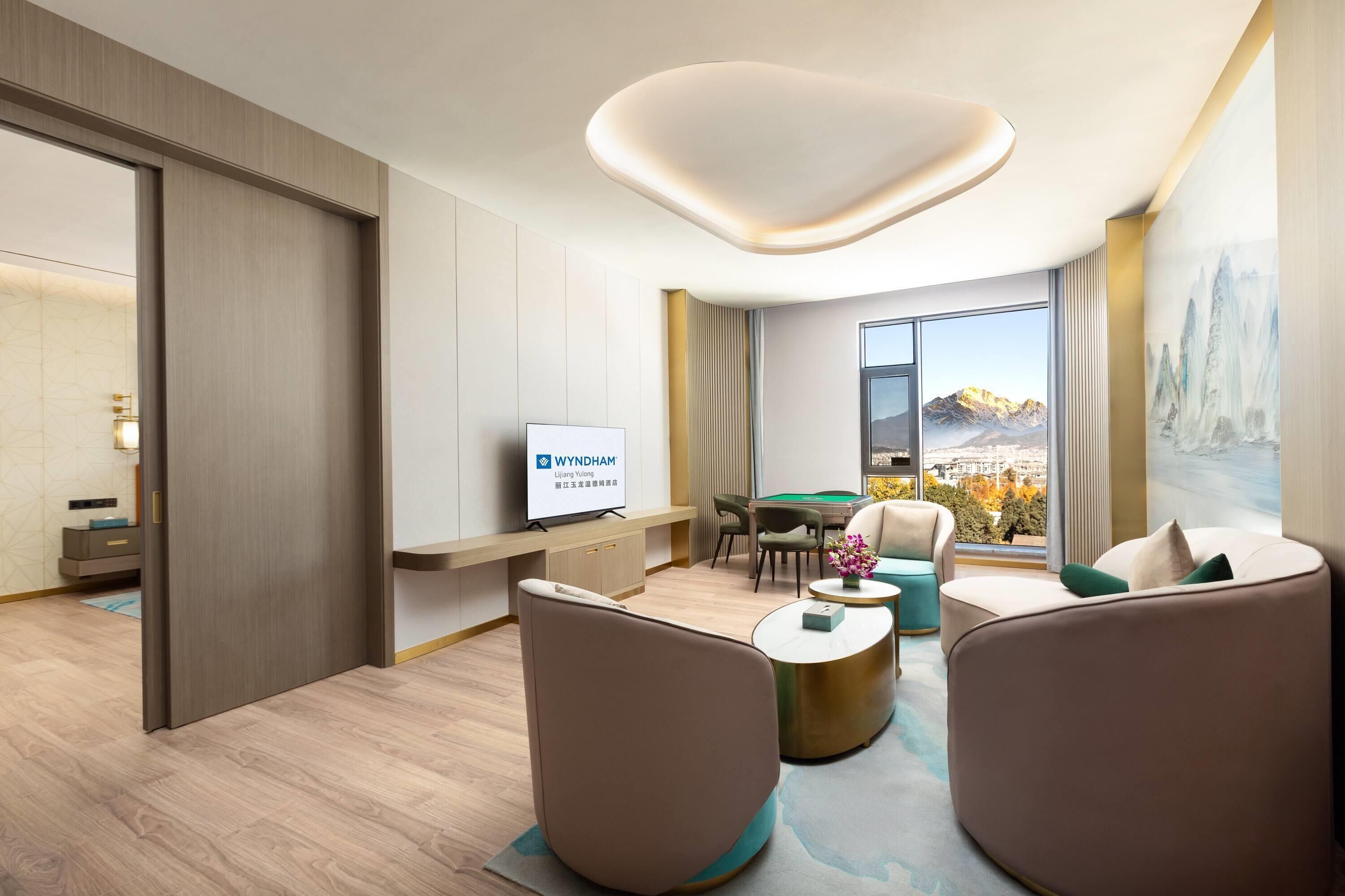 A modern hotel room with a pool table, comfortable seating, a flat-screen TV, and a large window with a mountain view.