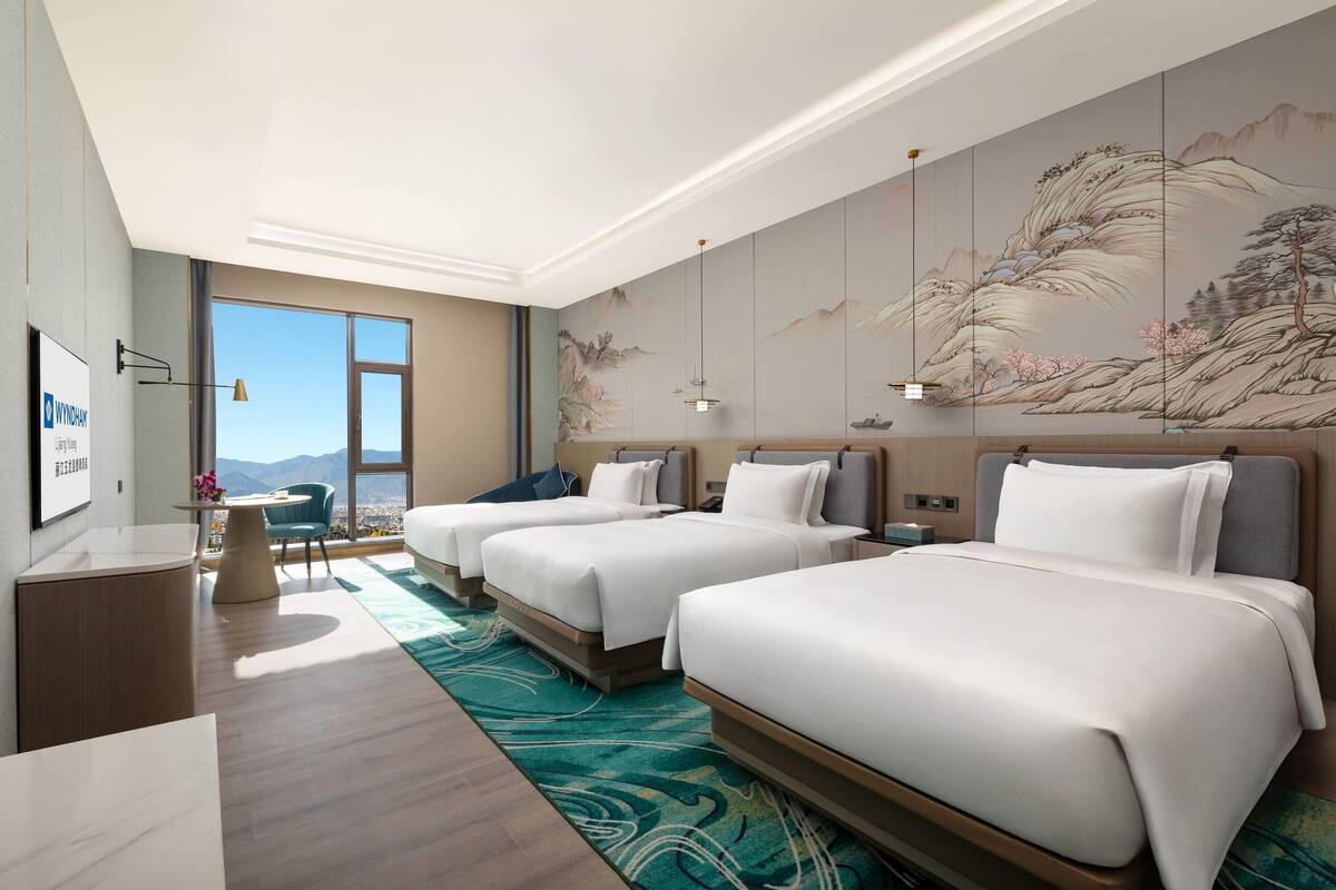 A hotel room with two beds, a desk, a chair, a large window, and a wall mural.