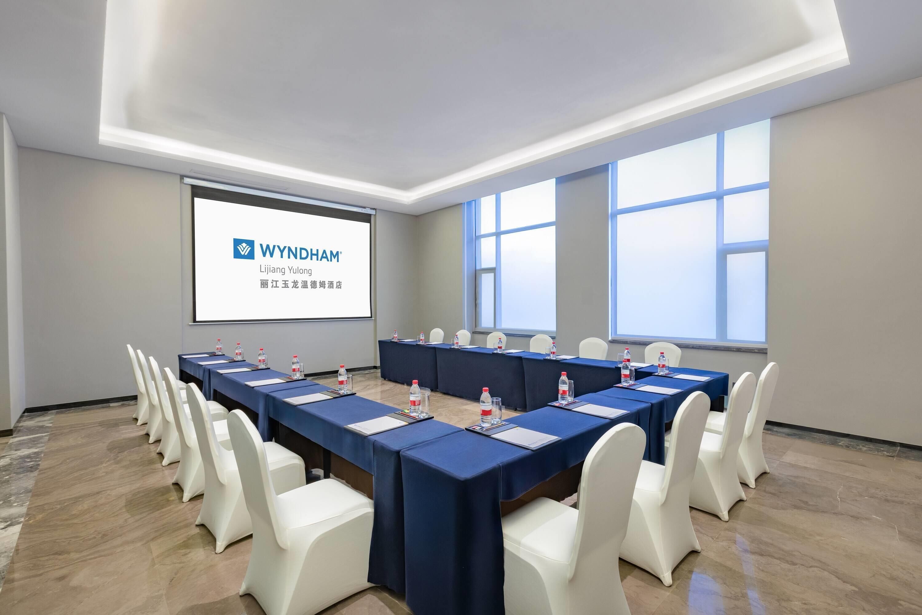 Un salón de conferencias con una larga mesa, sillas blancas y una pantalla proyectora que muestra WYNDHAM.