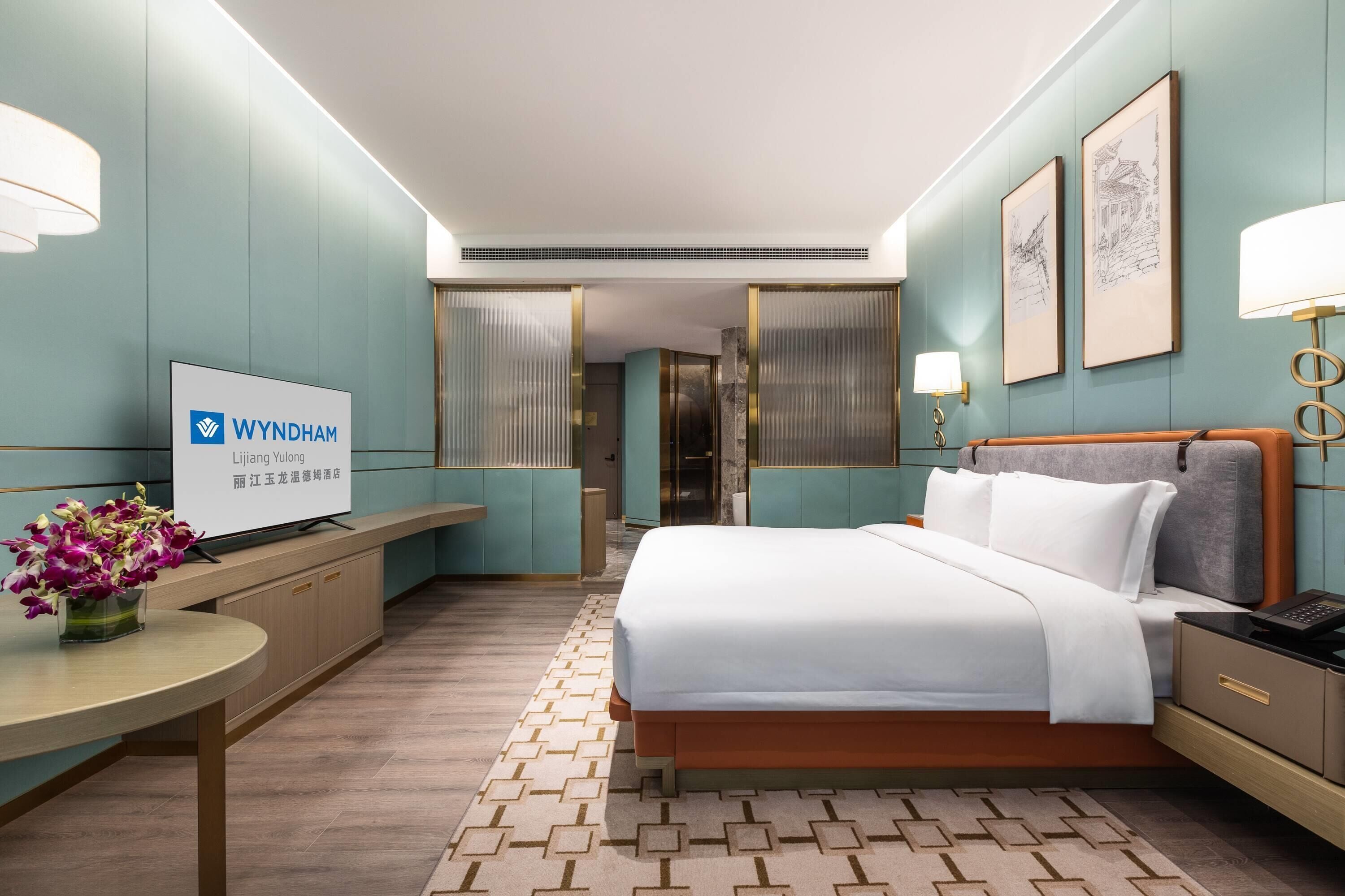 Una habitación de hotel con cama, mesita de noche, lámpara y un cartel con el nombre del hotel.
