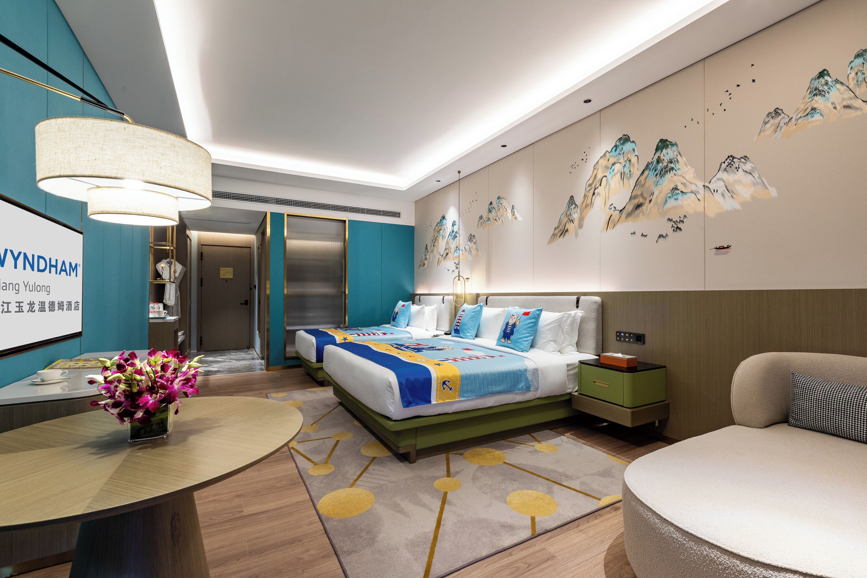 A hotel room with a bed, a desk, a chair, and a wall with artwork.