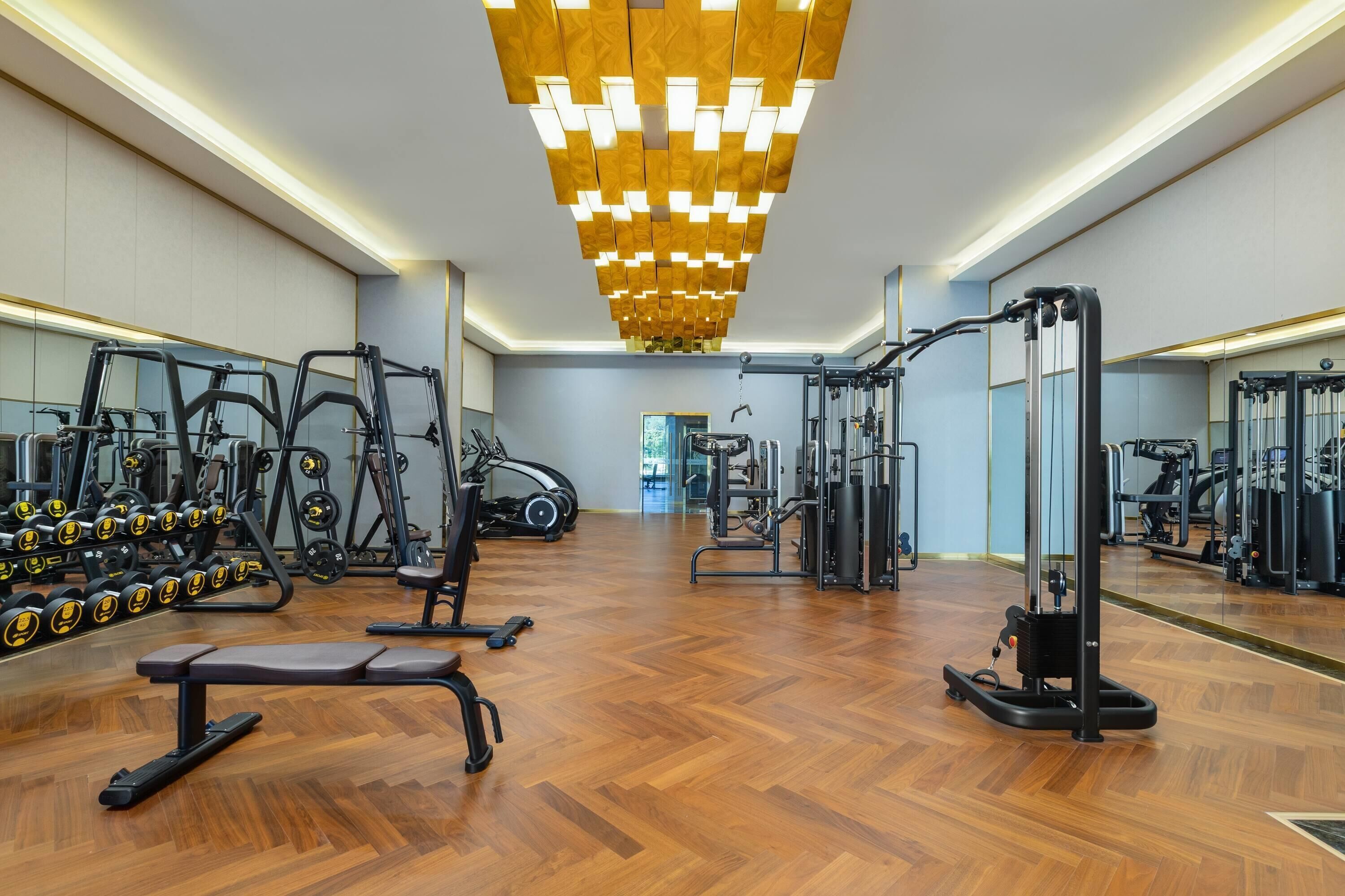 A gym with exercise equipment, wooden flooring, and a modern ceiling design.