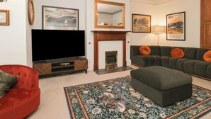 A living room with a flat-screen TV, a fireplace, a sofa, and a red armchair. - Norwood House (Ambleside)