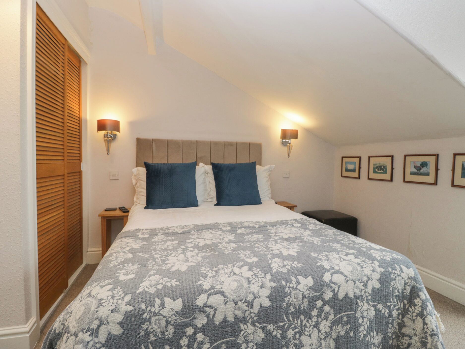 A bedroom with a large bed, two wall-mounted lamps, a wooden headboard, and a window with blinds.