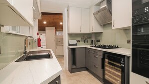 A modern kitchen with white cabinets, a stainless steel sink, a gas stove, and a built-in oven. - Norwood House (Ambleside)