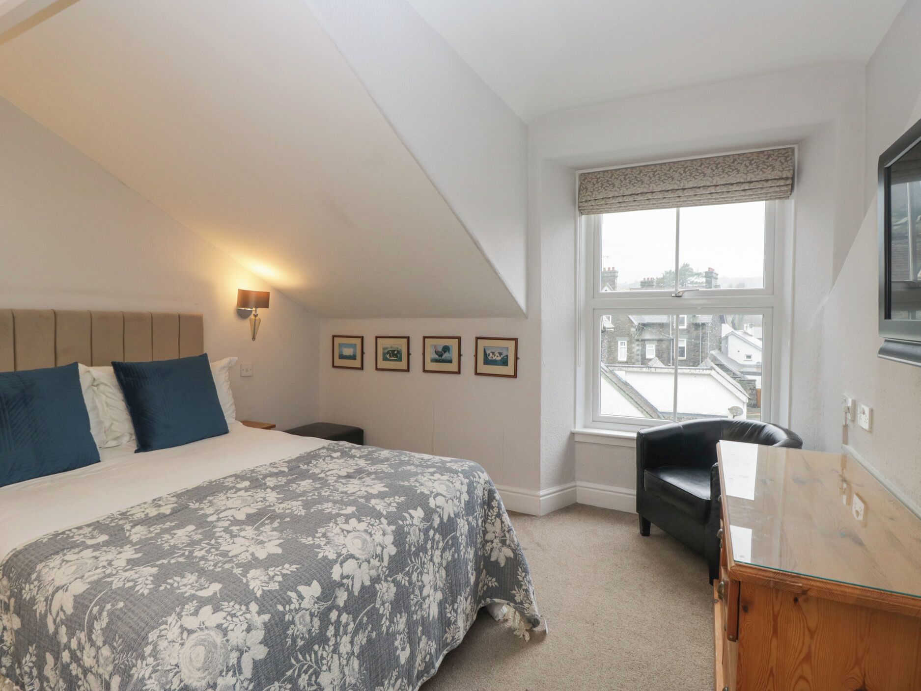 A bedroom with a bed, a desk, a chair, and a window with a view of buildings.