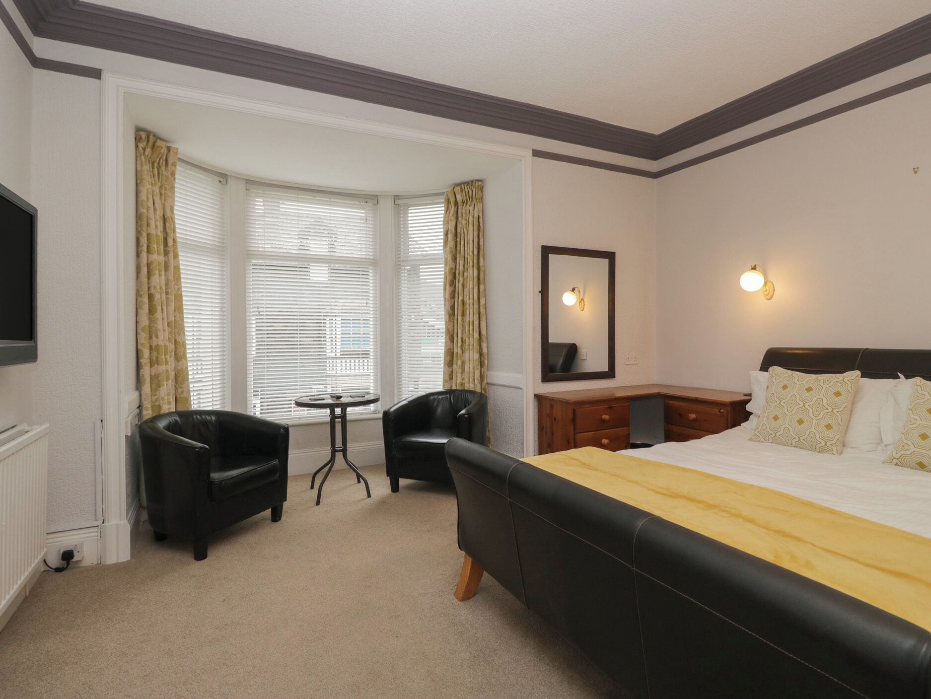 Een hotelkamer met een groot bed, een bureau, twee stoelen, een tafeltje, een spiegel en een televisie.