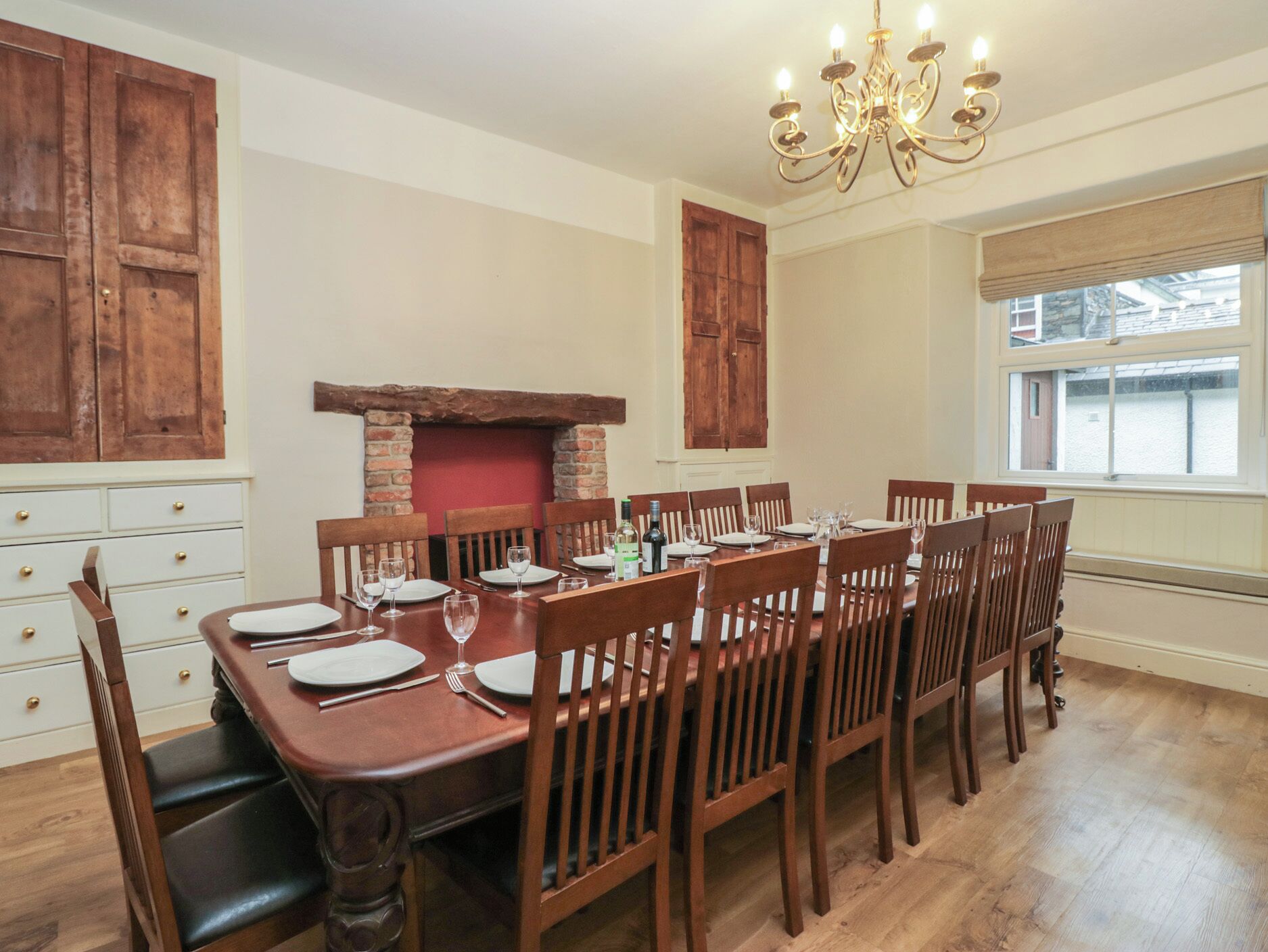 Ein Esszimmer mit einem langen Holztisch, gedeckt für sechs Personen, flankiert von Holzschränken und einem Kamin aus Ziegelsteinen.