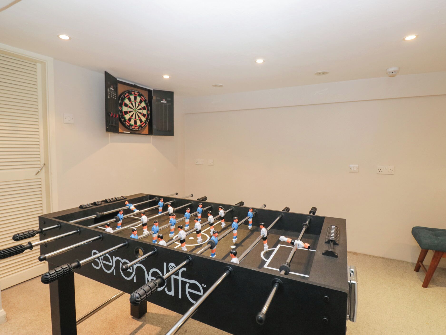 Une table de baby-foot dans une pièce où est accroché un jeu de fléchettes au mur.