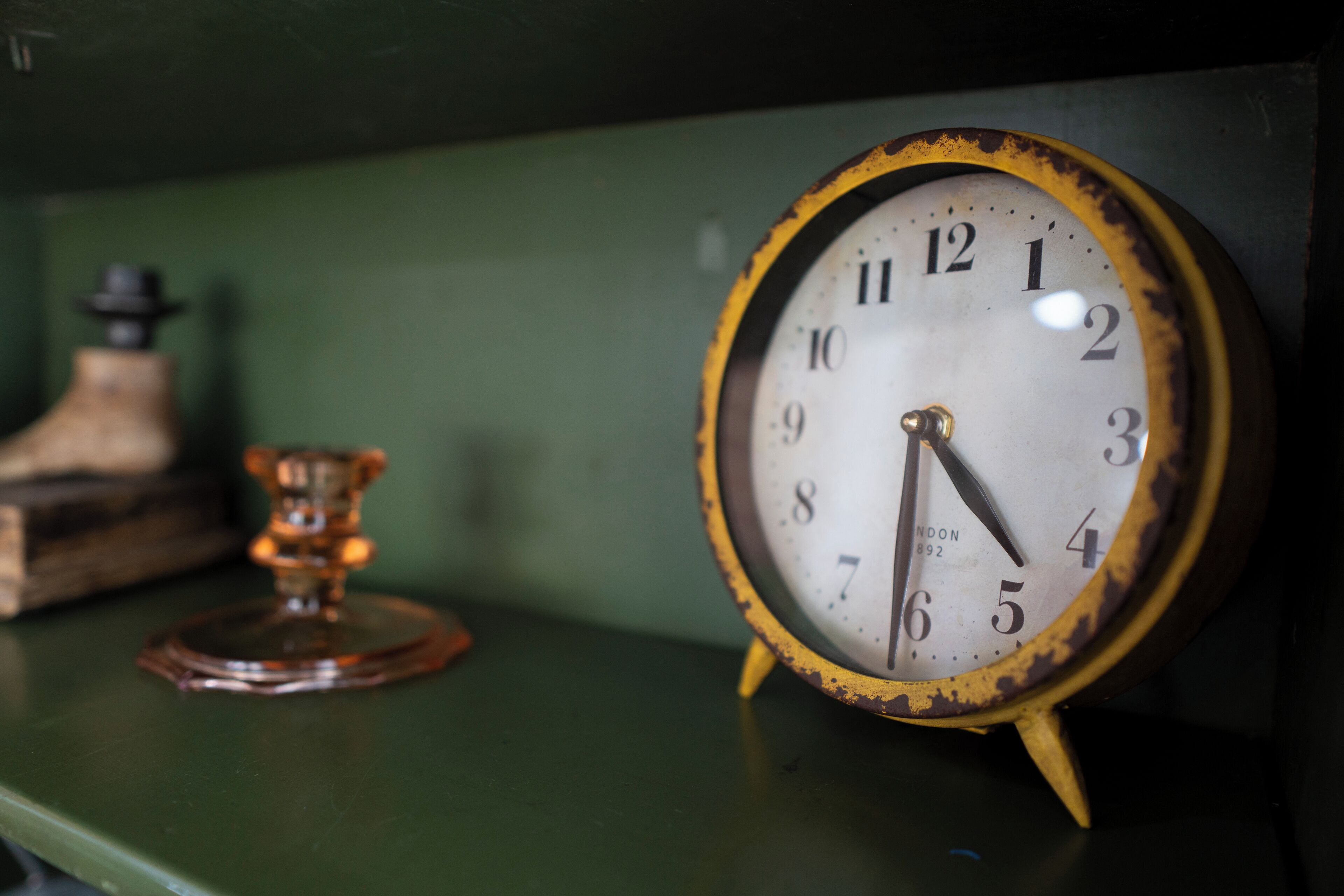 A vintage clock with a rustic frame and a brass pendulum, placed on a green surface.