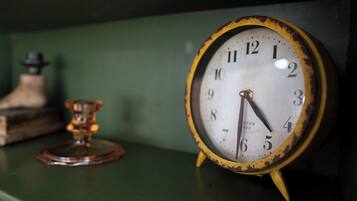 A vintage clock with a rustic frame and a brass pendulum, placed on a green surface.
