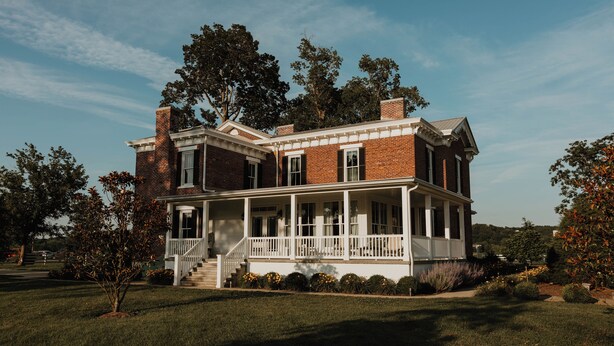A two-story brick house with a front porch and a covered front entrance. - Historic Woodlawn Estate: Where Historic Charm meets Modern Luxury (Fraziers Bottom)