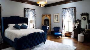 A bedroom with a large bed, a blue armchair, a mirror, and a chandelier. - Historic Woodlawn Estate: Where Historic Charm meets Modern Luxury (Fraziers Bottom)