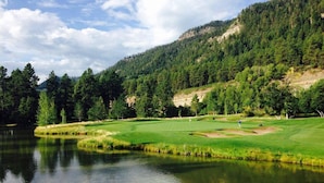 Un parcours de golf avec un lac, entouré d’une forêt dense et de collines.
