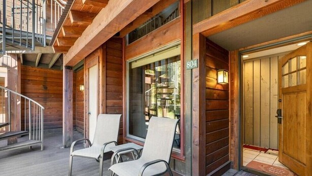 Une cabane en bois avec une véranda, deux chaises et un escalier.