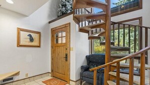 Une pièce spacieuse avec un escalier en bois, une porte, un tableau encadré et une chaise.
