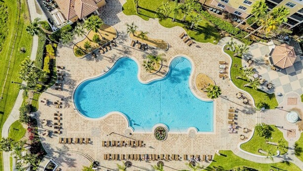An aerial view of a resort with a large central pool, multiple lounge areas, and surrounding greenery. - Epic 3-bed/3bth condo Next Door to Disney World (Orlando)