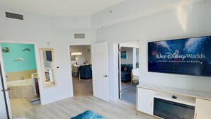 A modern hotel room with a large flat-screen TV, a blue shag rug, and a view into the dining area. - Epic 3-bed/3bth condo Next Door to Disney World (Orlando)