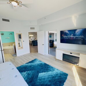 Habitación de hotel moderna con un televisor de pantalla plana grande, una alfombra mullida azul y vistas al comedor.
