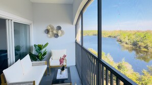 A balcony with a view of a lake, furnished with two white sofas and a table with a vase of flowers. - Epic 3-bed/3bth condo Next Door to Disney World (Orlando)