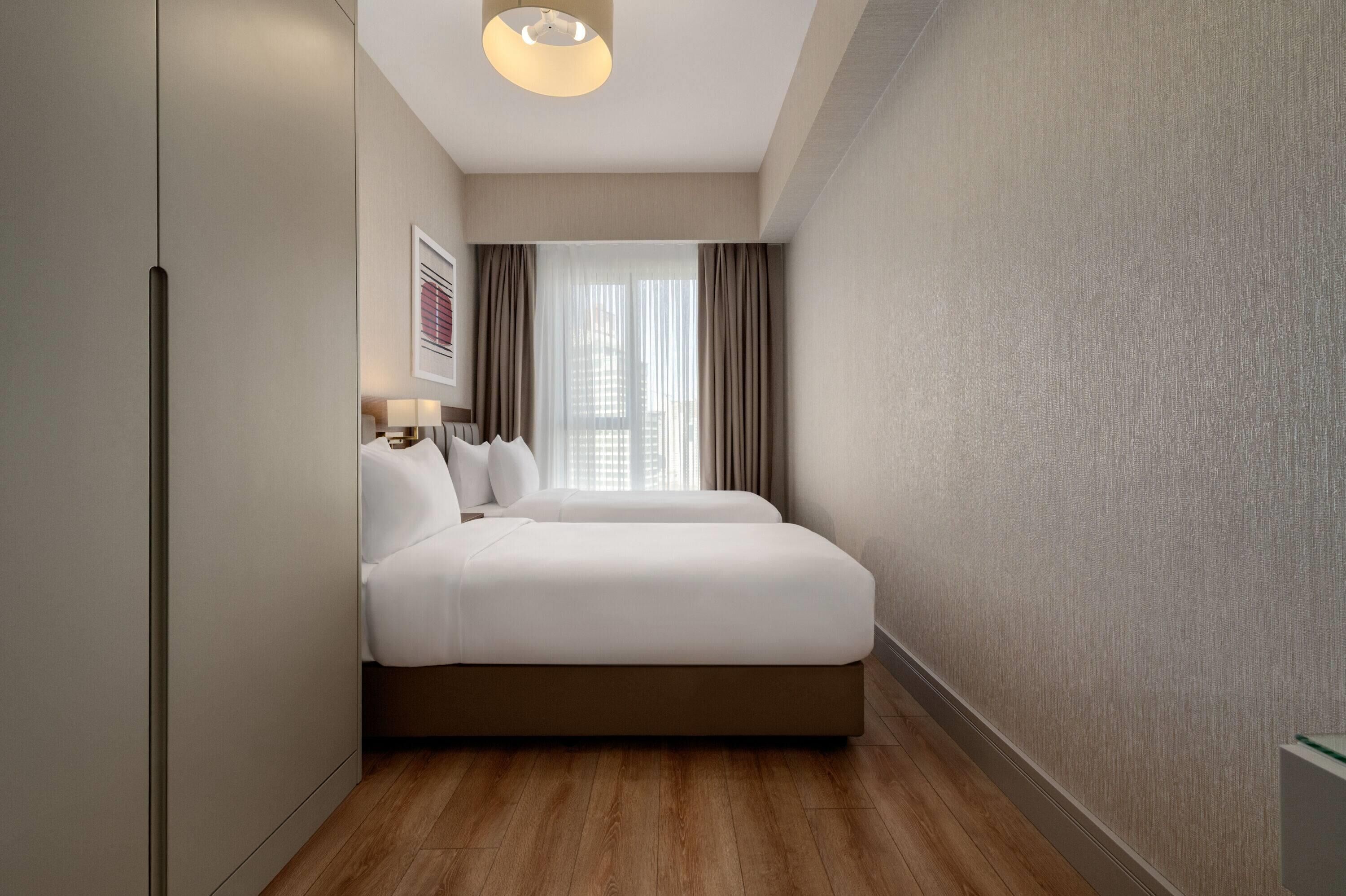 Een hotelkamer met een bed, een nachtkastje, een lamp, een raam met gordijnen en een aan de muur hangend schilderij.