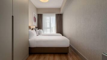 Een hotelkamer met een bed, een nachtkastje, een lamp, een raam met gordijnen en een aan de muur hangend schilderij.