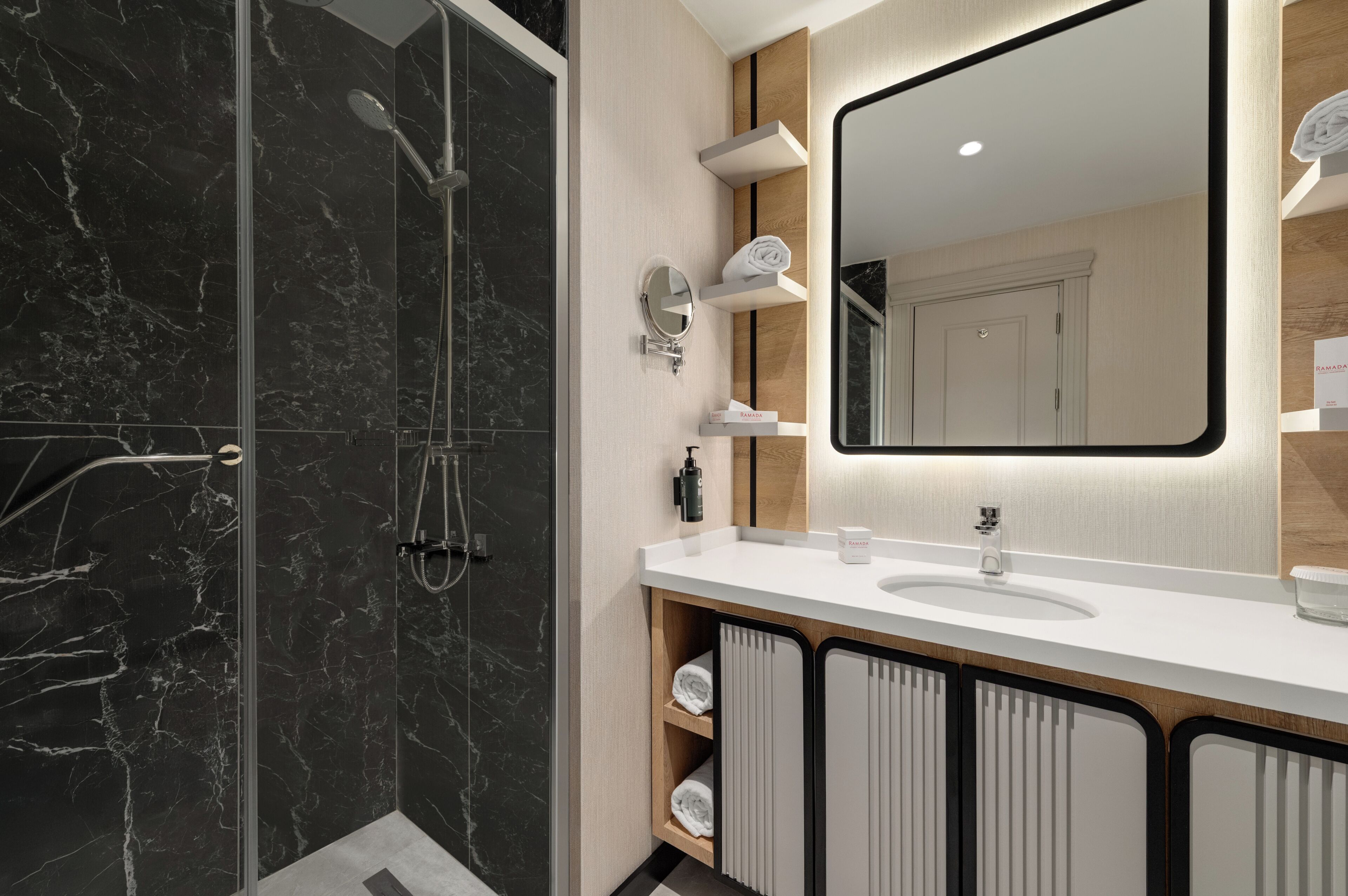A modern bathroom with a glass-enclosed shower, a large mirror, and a white sink with a wooden cabinet.